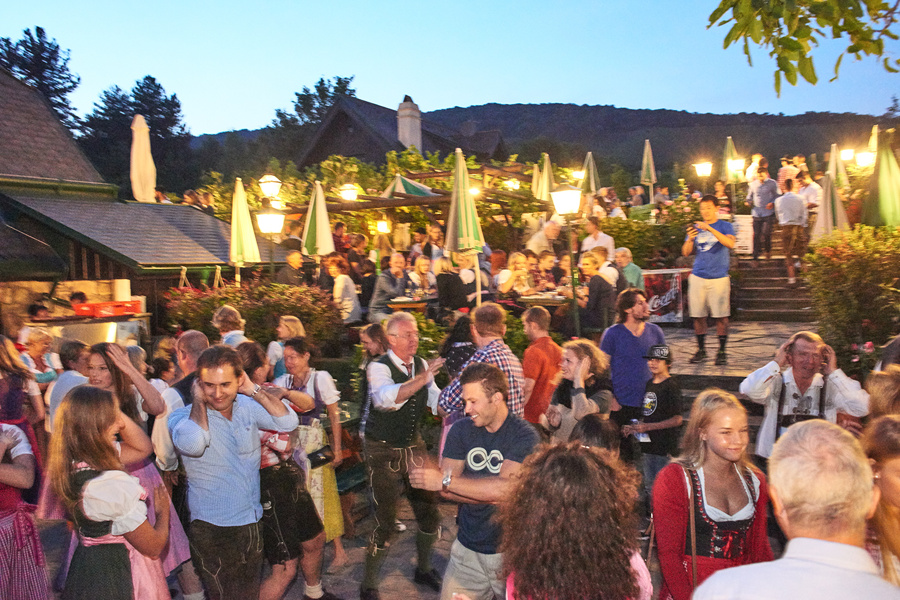 Ein lebhaftes Fest unter freiem Himmel mit Menschen, die sich in der Abenddämmerung treffen, einige in traditioneller bayerischer Kleidung.