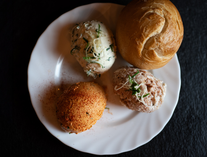 Ein weißer Teller mit einem Brötchen und drei Löffeln aromatisierter Butter oder Aufstrich, garniert mit Kräutern.