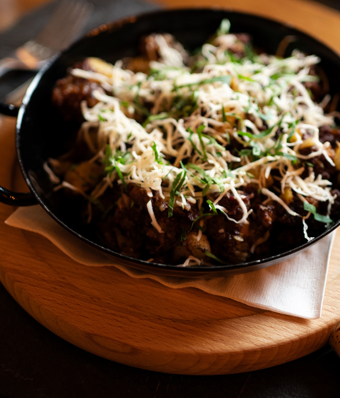 Eine schwarze Pfanne mit einem überbackenen Käseteller, garniert mit Kräutern, auf einem Holzbrett.