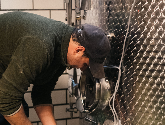 Eine Person mit Kappe inspiziert einen Edelstahltank in einer industriellen Umgebung mit gefliesten Wänden.