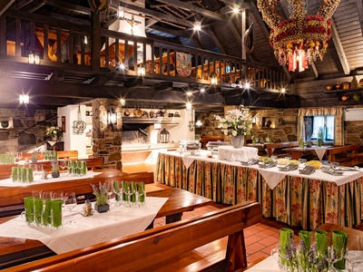 Rustikales Restaurant mit Holzbalken, gedeckten Tischen, Blumenschmuck und einem großen dekorativen Kronleuchter.