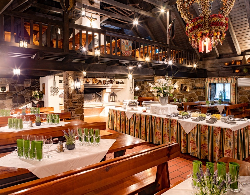 Buschenschank Fuhrgassl-Huber | Wiener Heuriger Rustikales Restaurant mit Holzbalken, gedeckten Tischen, Blumenschmuck und einem großen dekorativen Kronleuchter.
