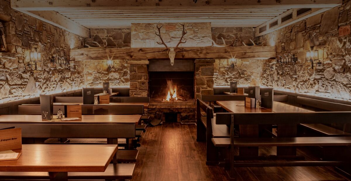 Rustikales Restaurant mit Holztischen, Steinwänden, einem Kamin und einem Geweih über dem Kaminsims.